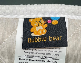 缝在床垫侧面的品牌织唛特写(CPSC 官方图):“Bubble bear”小熊图案,下沿可见生产日期 04/2022 与部分地址信息