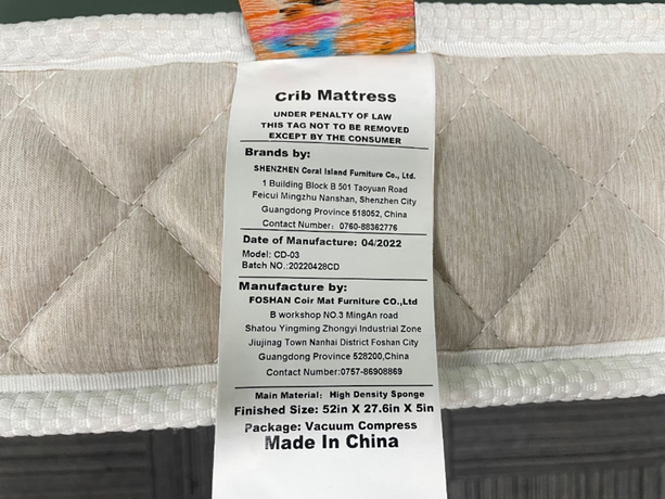 Gray Style(CD-03)的法律标签正面(CPSC 官方图):顶部印“crib Mattress / UNDER PENALTY OF LAW / THIS TAG NOT TO BE REMOVED EXCEPT BY THE CONSUMER”;“Brands by”为深圳珊瑚岛家具(深圳南山地址、邮编 518052);“Date of Manufacture: 04/2022”“Model: CD-03”“Batch: 20220428CD”;“Manufacture by”为 FOSHAN Coir Mat Furniture(佛山南海九江镇地址);下方为主材料、成品尺寸、真空压缩包装与 Made in China