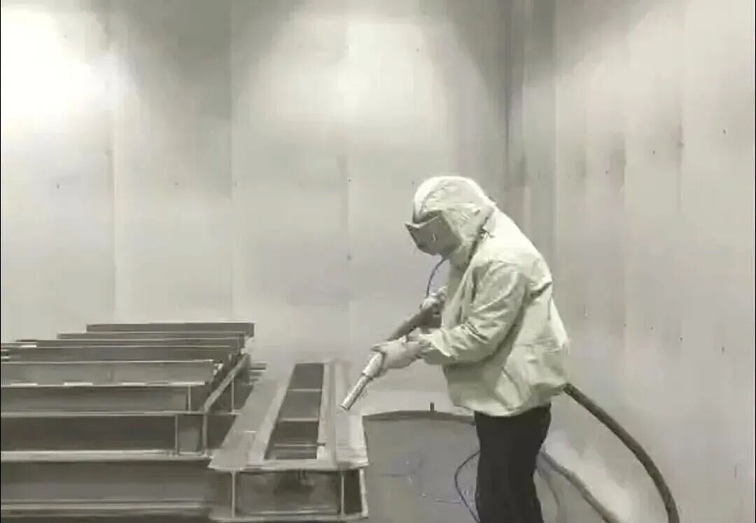 喷砂房内的作业现场:操作人员穿戴防护装备对钢构件进行喷砂
