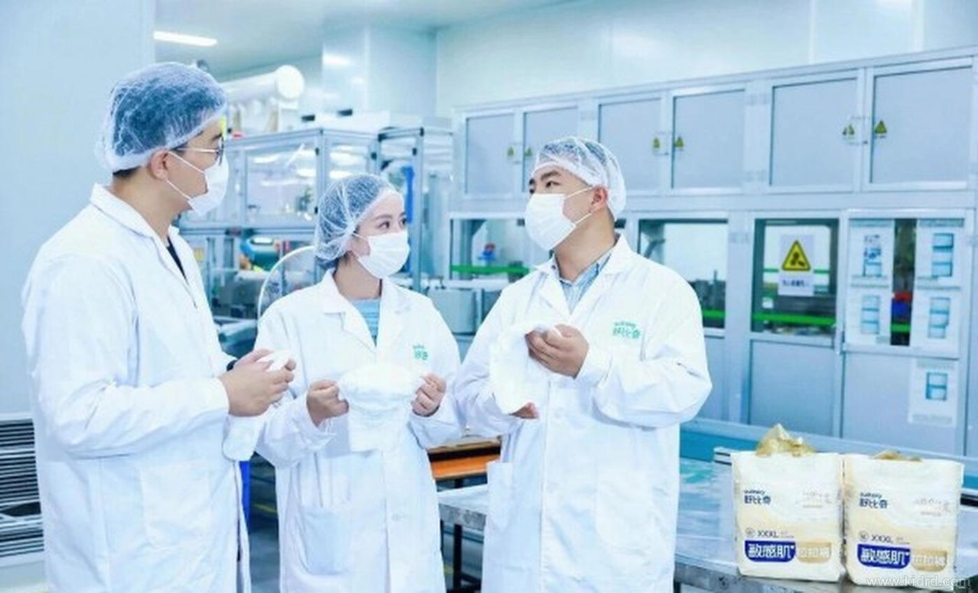 身着洁净服、口罩与发帽的工程师在洁净车间内交流,手中为舒比奇敏感肌纸尿裤产品