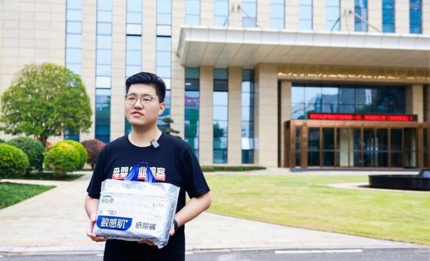 舒比奇自有工厂园区大门前,参观者手持舒比奇敏感肌纸尿裤产品包装